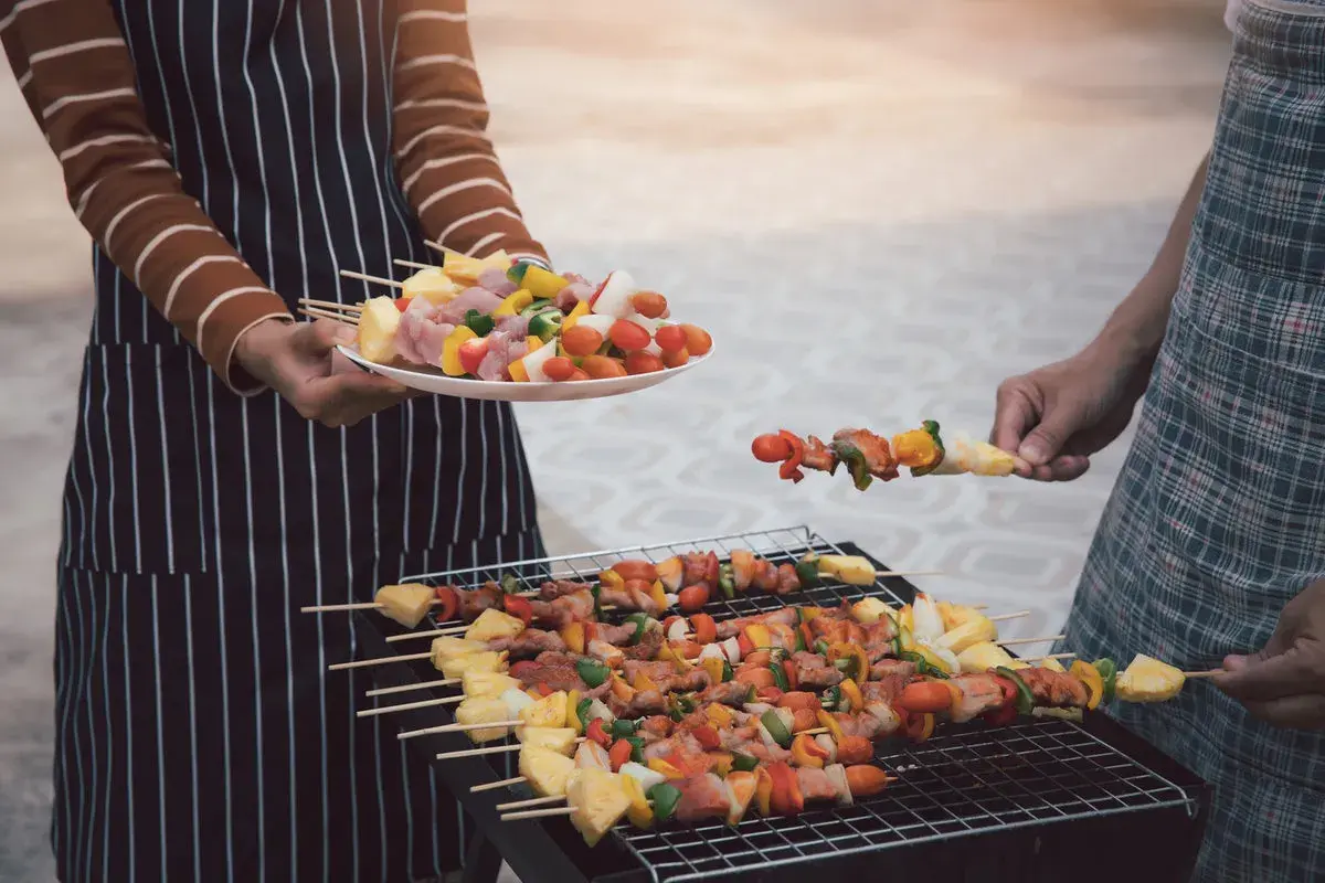 Ludzie grillują szaszłyki z mięsem i warzywami na grillu.