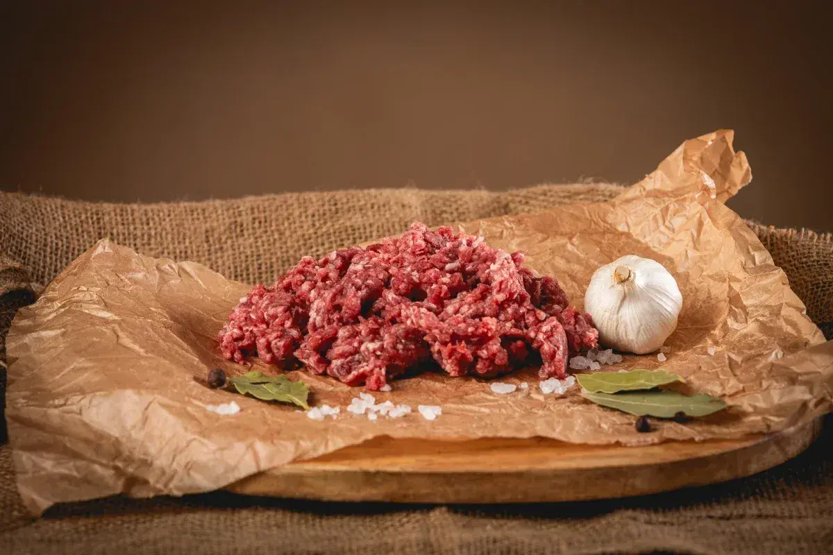 Świeże, mielone mięso wołowe, idealne na soczyste burgery. Obok czosnek, sól, liście laurowe i pieprz.
