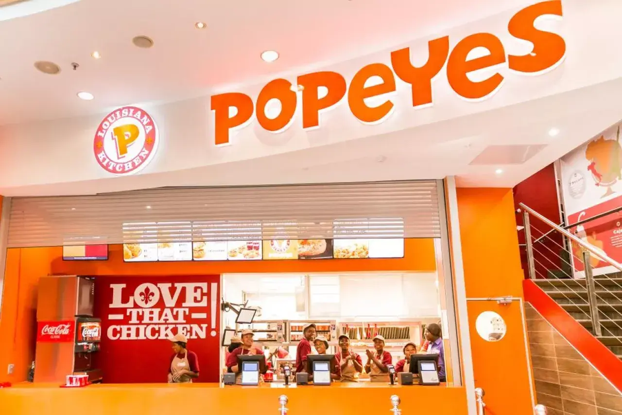 Wnętrze restauracji Popeyes Polska. Pracownicy za ladą, logo "Love That Chicken" i menu.