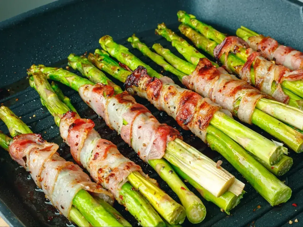 Zielone szparagi owinięte w boczek, grillowane na patelni. Pyszne szparagi z grilla gotowe do podania.