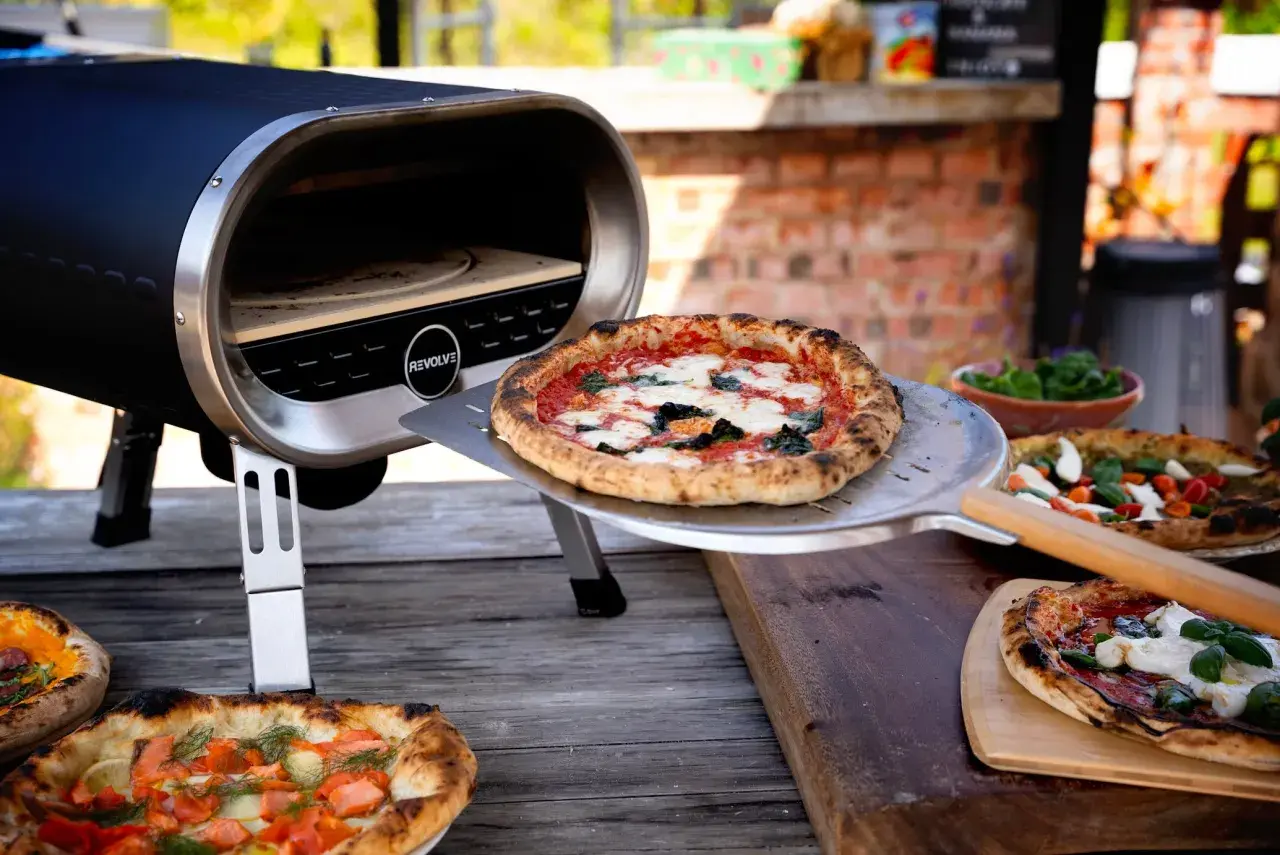 Piec do pizzy z otwartą komorą, na stole leżą świeżo upieczone pizze.