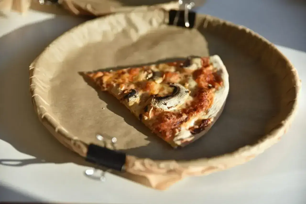 Kawałek pizzy z pieczarkami na papierowym talerzu. Zastanawiasz się nad pizza kcal?