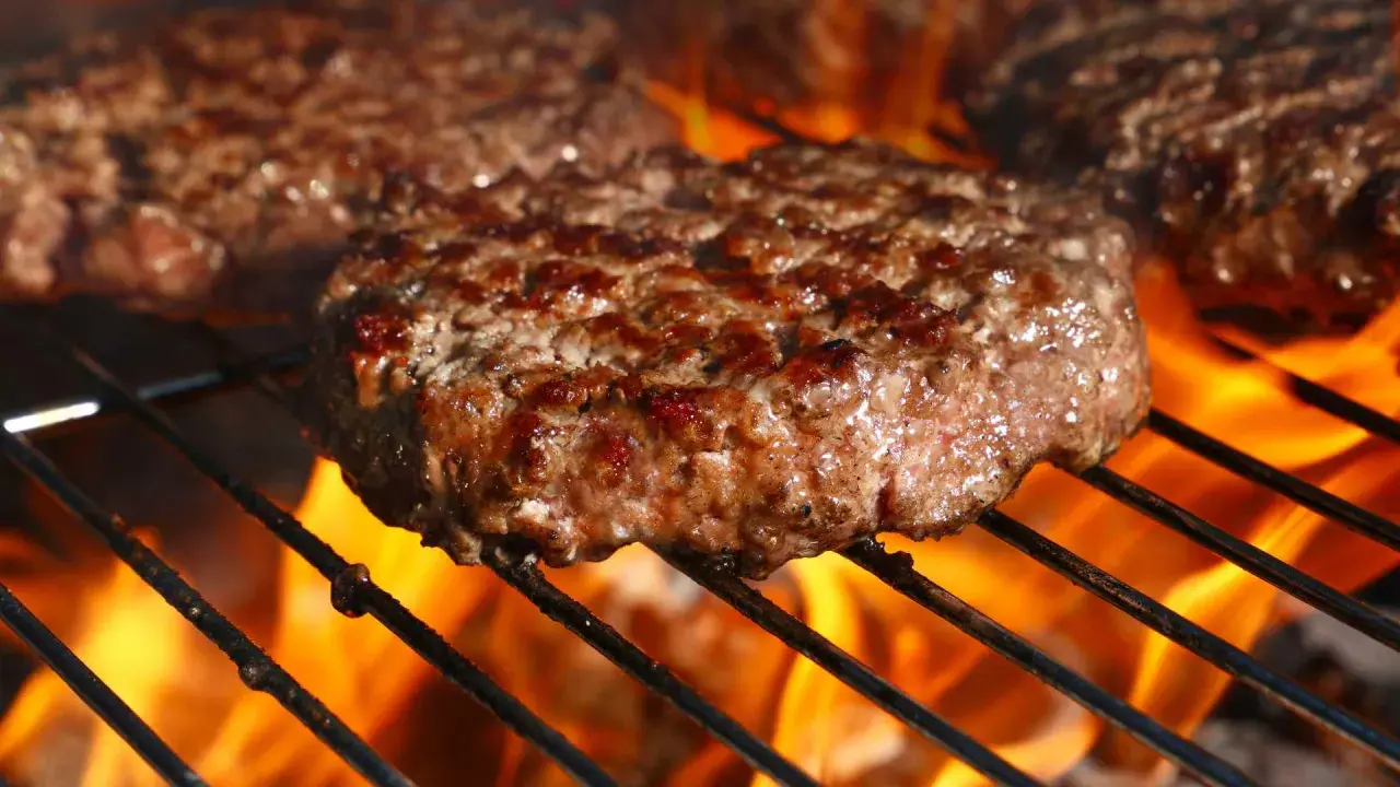 Soczyste kotlety mielone smażące się na grillu z płomieniami.