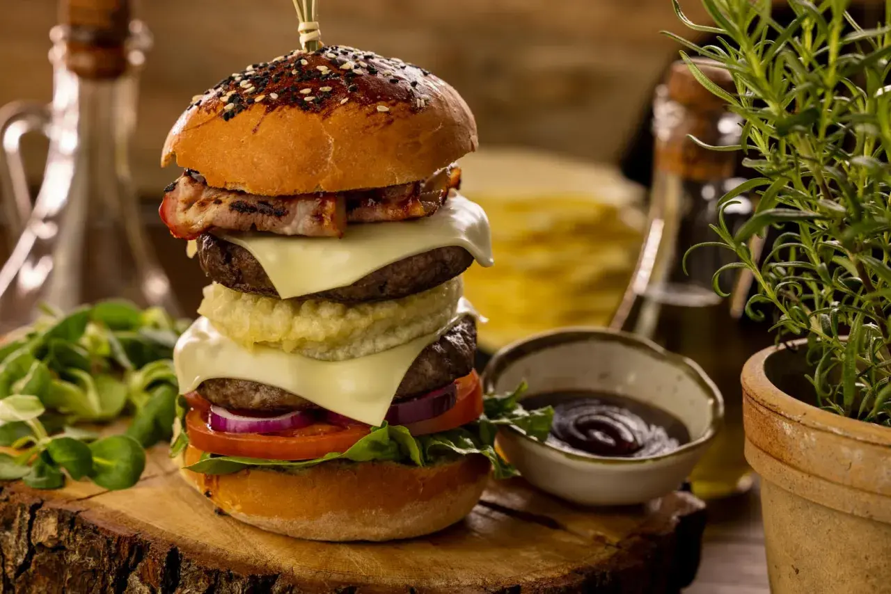 Wielowarstwowy burger wołowy z bekonem, serem, warzywami i sosem na drewnianej desce.