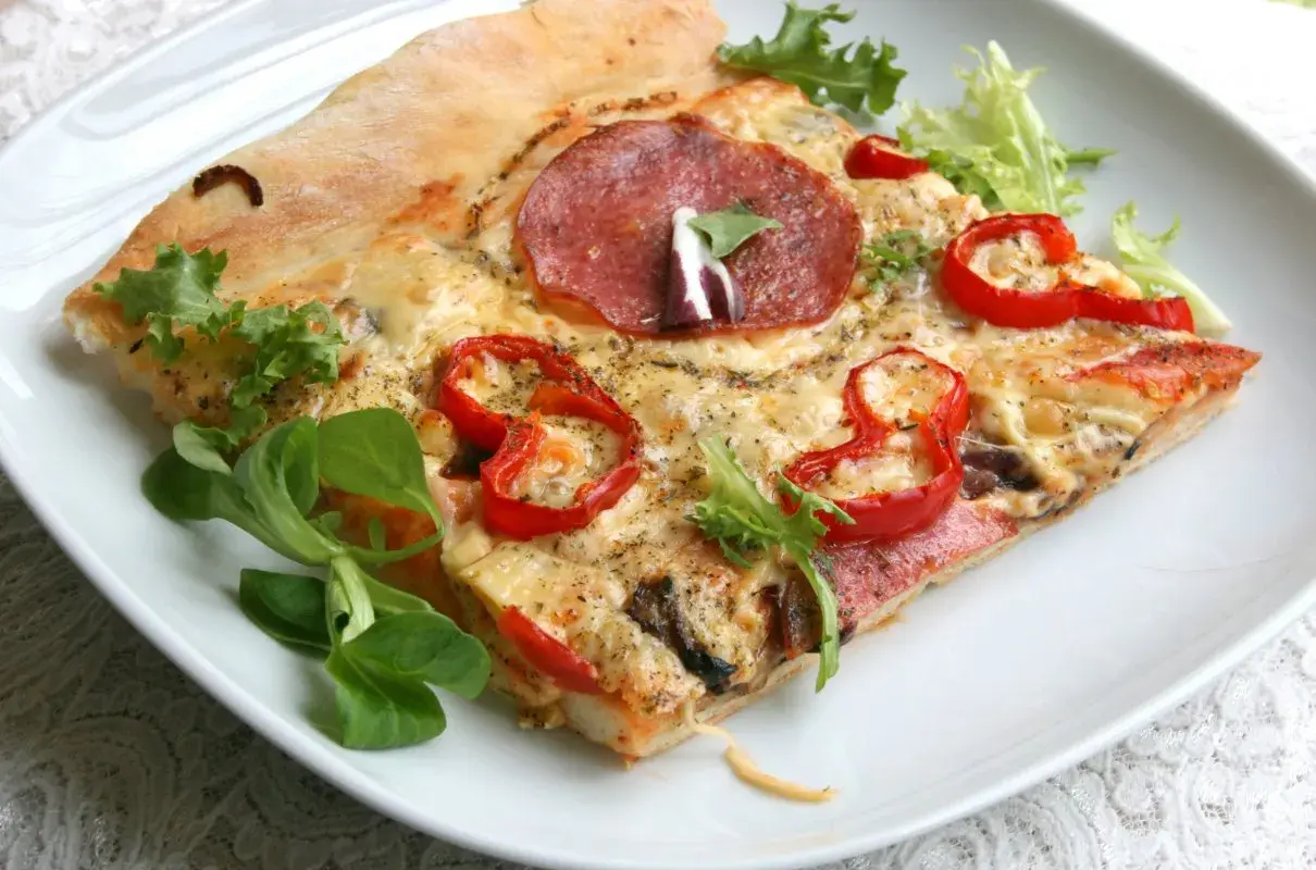 Kawałek pizzy z salami, papryką i serem na białym talerzu.