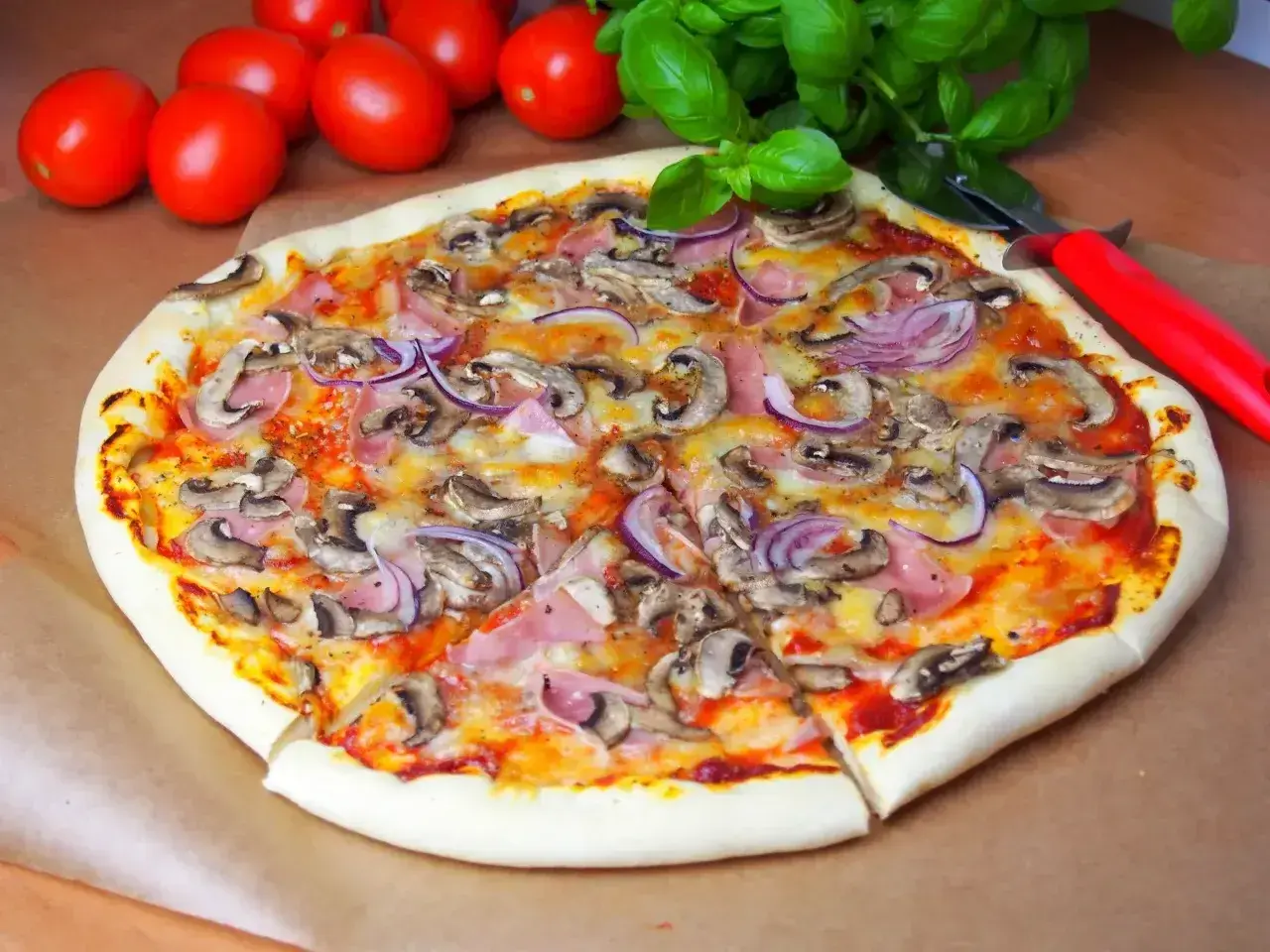 Pyszna pizza capriciosa z pieczarkami, szynką i czerwoną cebulą, gotowa do pokrojenia.