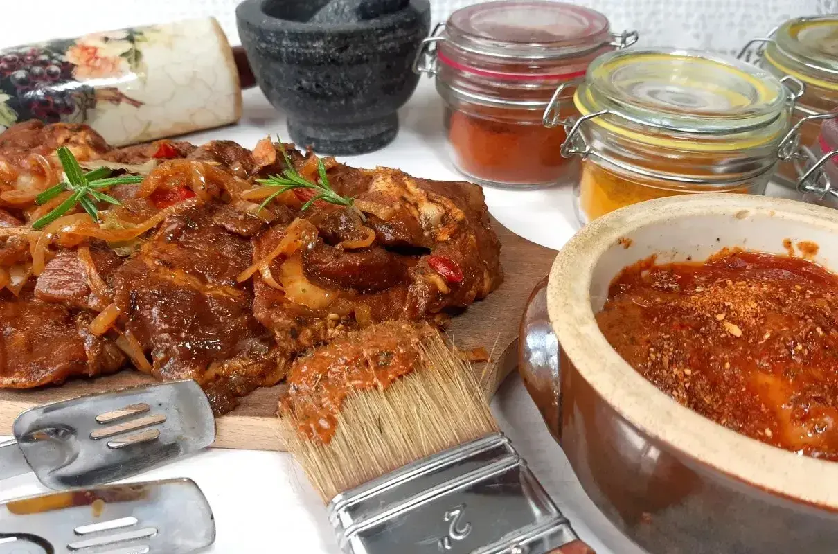 Karkówka na grilla w aromatycznej marynacie, gotowa do pieczenia. Obok pędzel z marynatą, przyprawy i narzędzia.