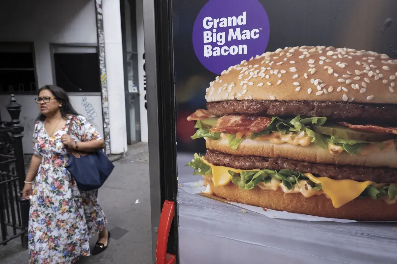 Reklama Grand Big Mac Bacon. Kobieta w kwiecistej sukience mija billboard z apetycznym burgerem.