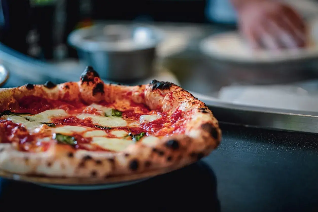 Puszysta pizza z serem i bazylią na ciemnym tle.