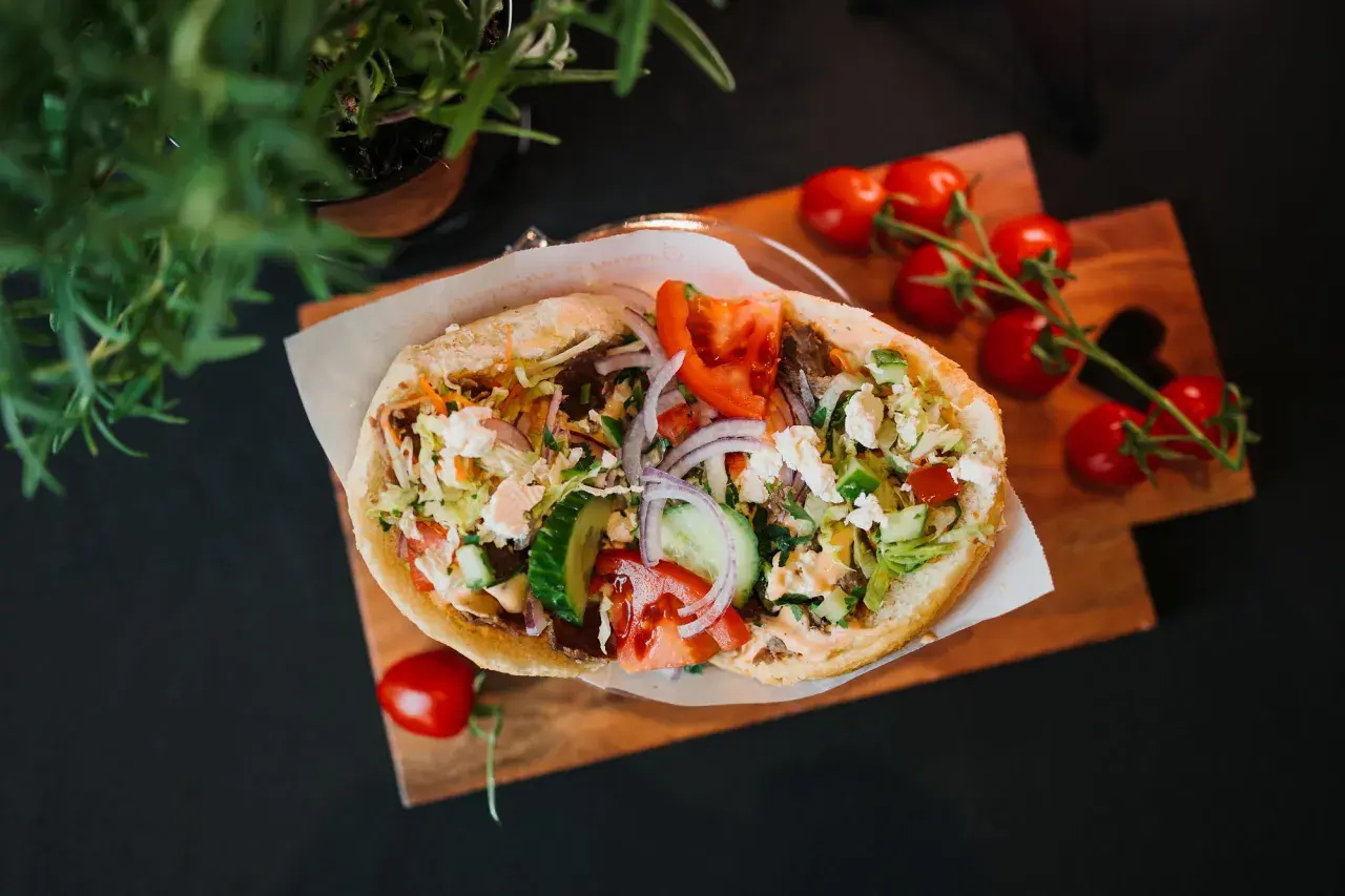 Pyszny kebab z warzywami i serem feta na desce, obok pomidorki i zielenina.