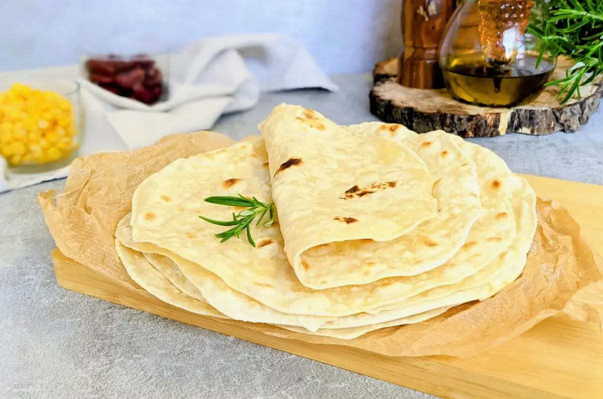 Stos świeżo upieczonych tortilli, idealnych do przygotowania najlepszej tortilli z ulubionymi dodatkami. Gałązka rozmarynu dodaje aromatu.