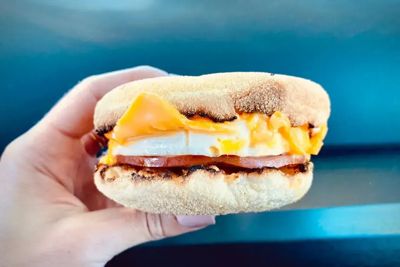 Mcmuffin farmerski z jajkiem, serem i szynką, trzymany w dłoni. Idealny na szybkie śniadanie.