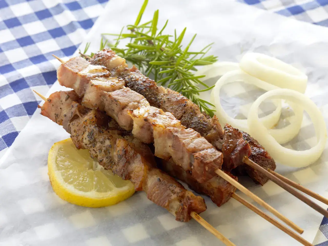 Aromatyczne souvlaki na patyczkach, podane z plasterkiem cytryny, gałązką rozmarynu i krążkami cebuli.