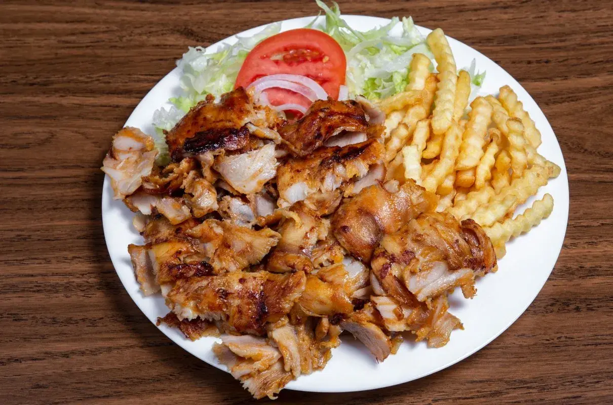Talerz z kurczakiem gyros, frytkami, sałatą, pomidorem i cebulą.