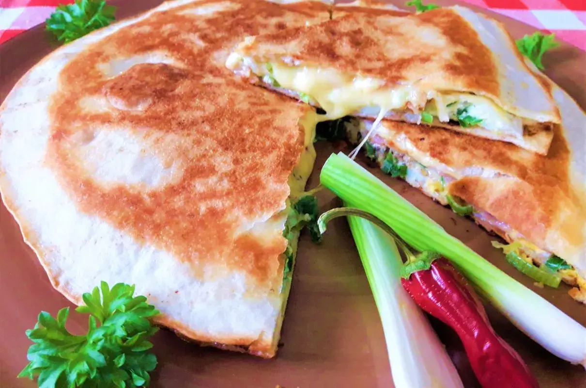 Złocista tortilla z jajkiem, serem i szynką, usmażona na patelni, z dodatkiem szczypiorku i papryczki.