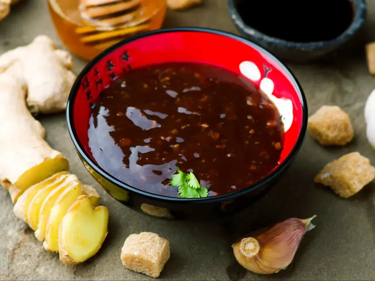 Miseczka z aromatycznym sosem teriyaki, obok świeży imbir, czosnek i brązowy cukier.