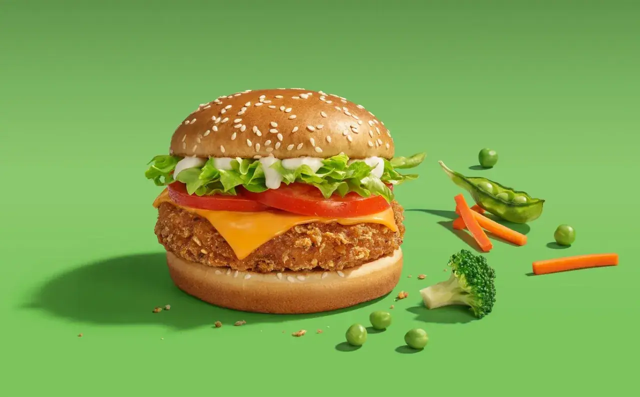 Pyszny wege burger McDonald's z chrupiącym kotletem, serem, pomidorem i sałatą. Obok świeże warzywa: groszek, marchewka i brokuł.