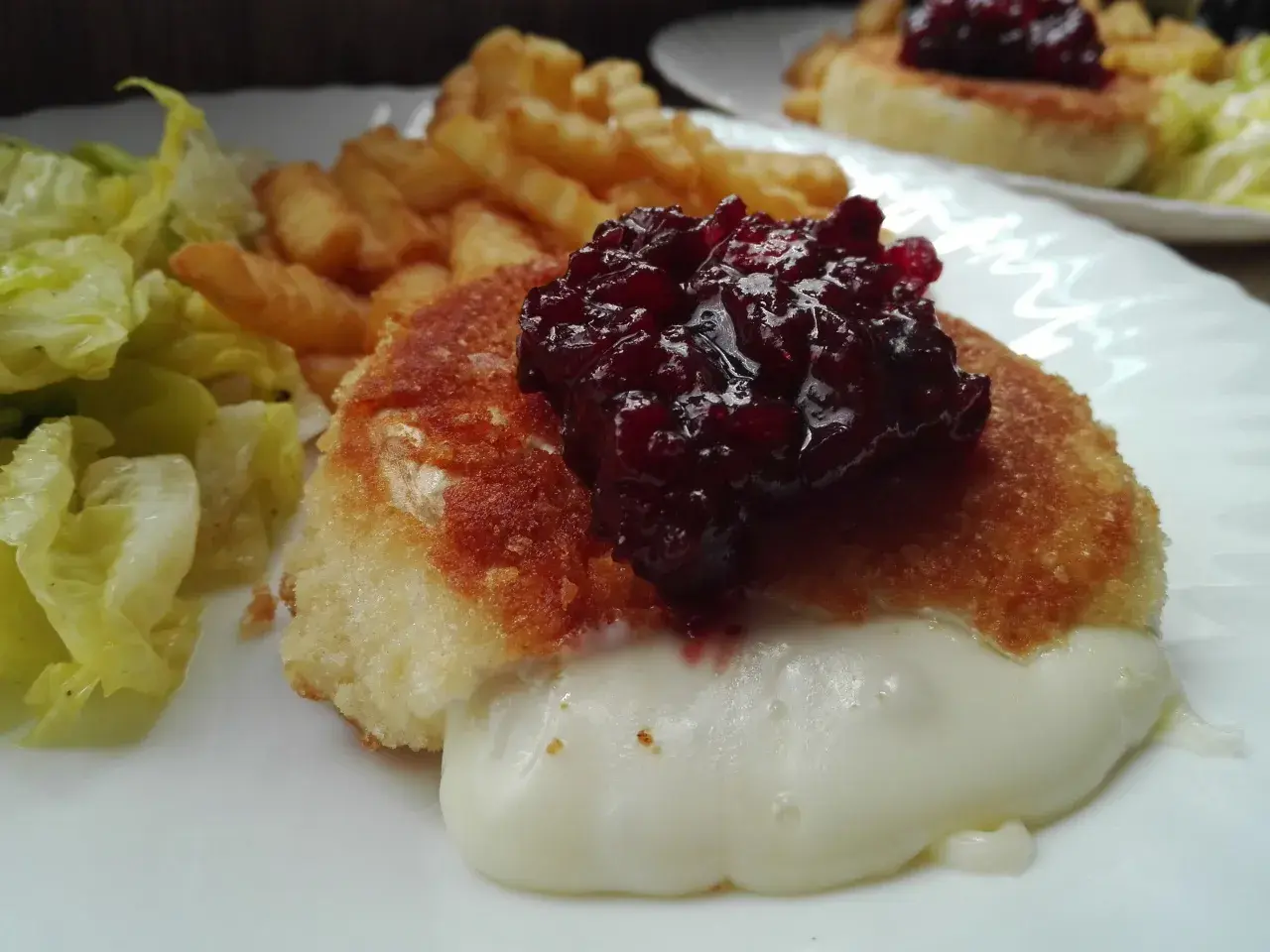 Pyszny camembert w panierce, z rozpływającym się serem, podany z frytkami i sałatką.