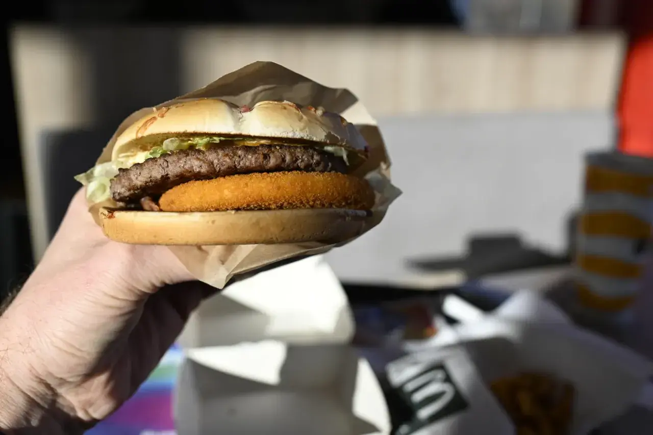 Dłoń trzyma burgera McDouble z podwójnym kotletem i chrupiącą warstwą.