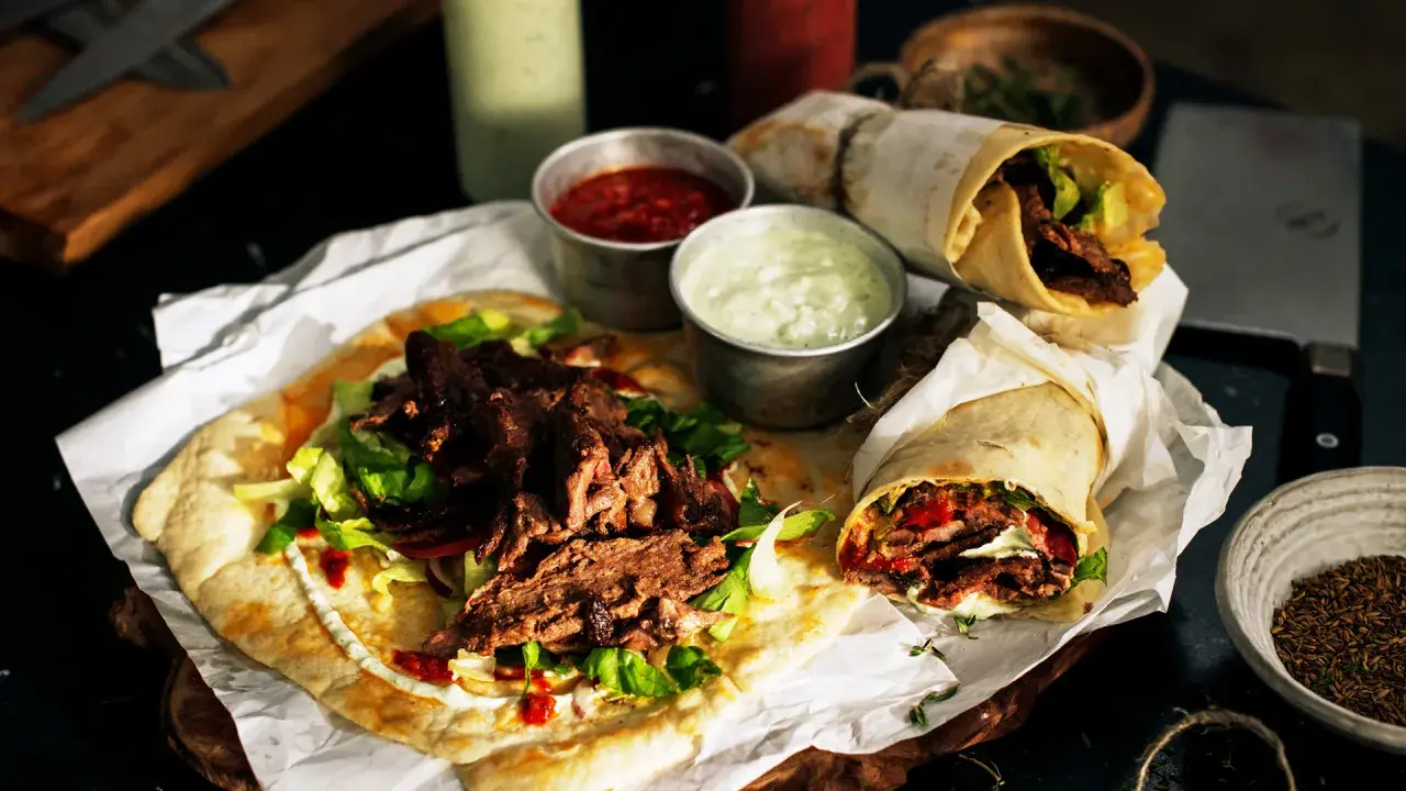 Pyszny lawasz kebab z soczystym mięsem, świeżą sałatą i sosami. Dwa zawinięte w papier i jeden otwarty na płaskim chlebie.