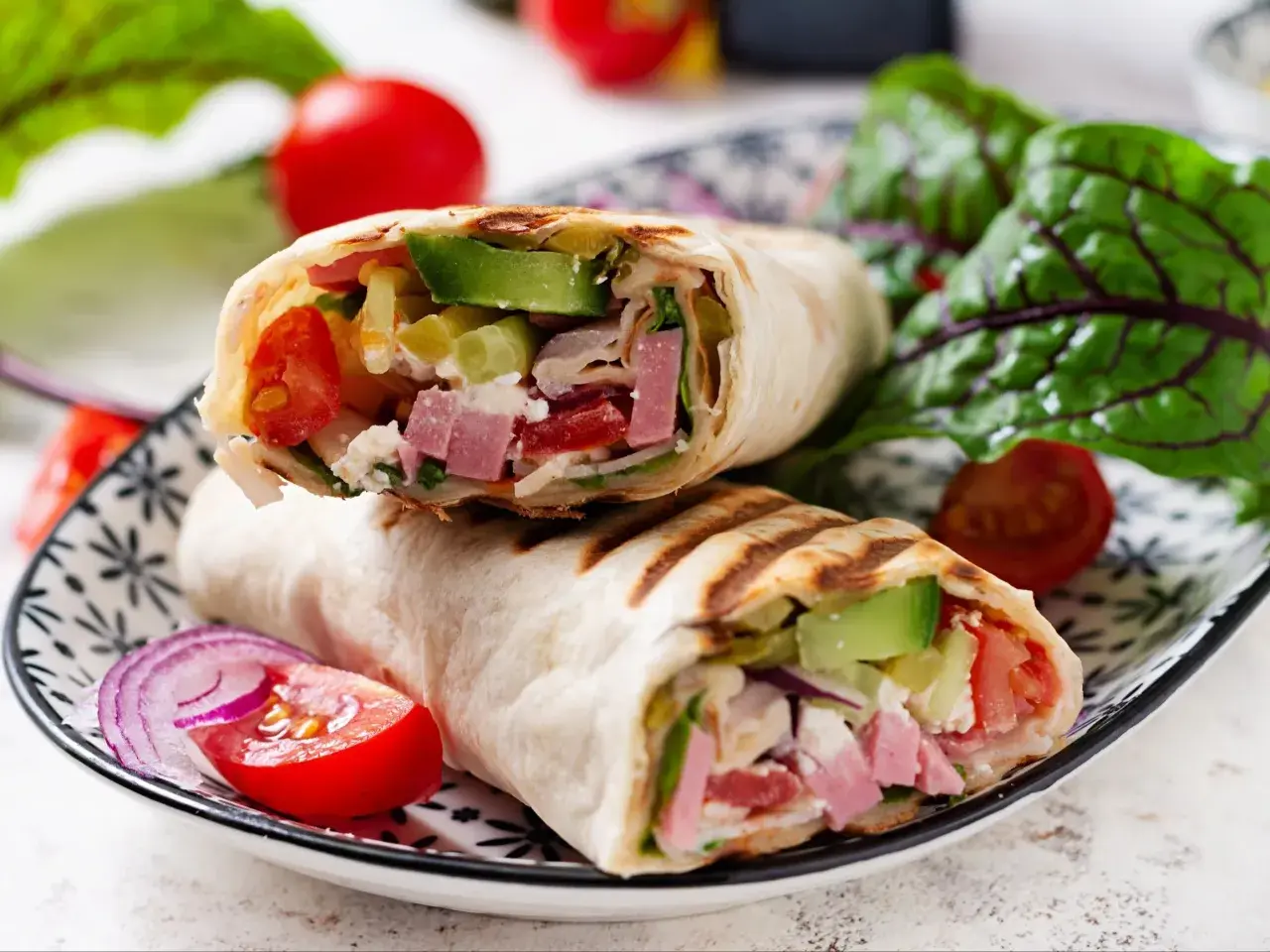 Pyszna tortilla z szynką i serem, pełna świeżych warzyw, podana na talerzu z pomidorkami i sałatą.