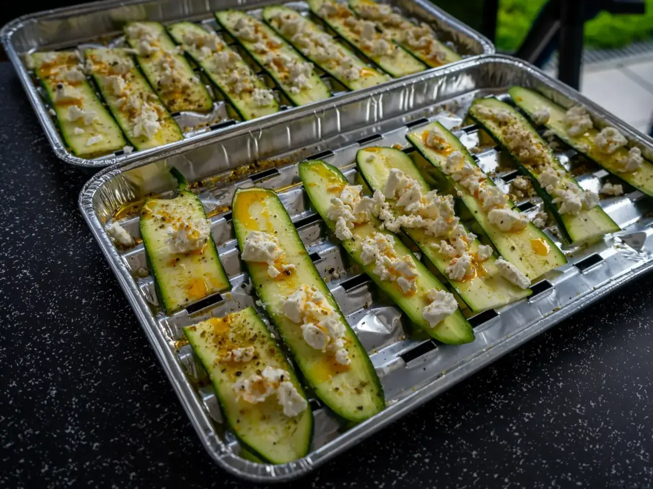 Półplasterki cukinii z serem feta i przyprawami, gotowe do grillowania.