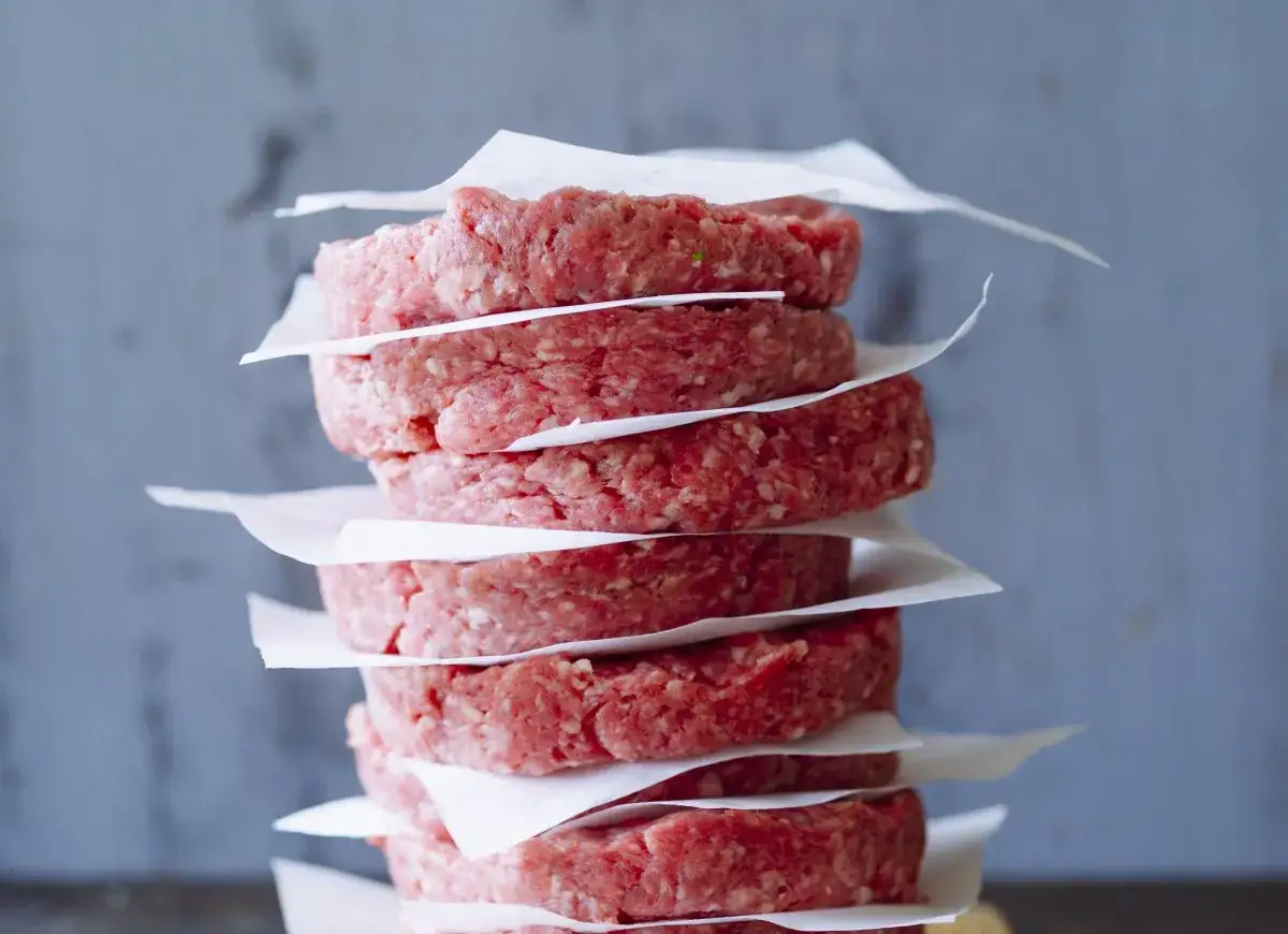 Stos surowych kotletów na hamburgery, każdy oddzielony papierem. Idealne do przygotowania pysznych burgerów, oto jak przyprawić mięso na hamburgery.