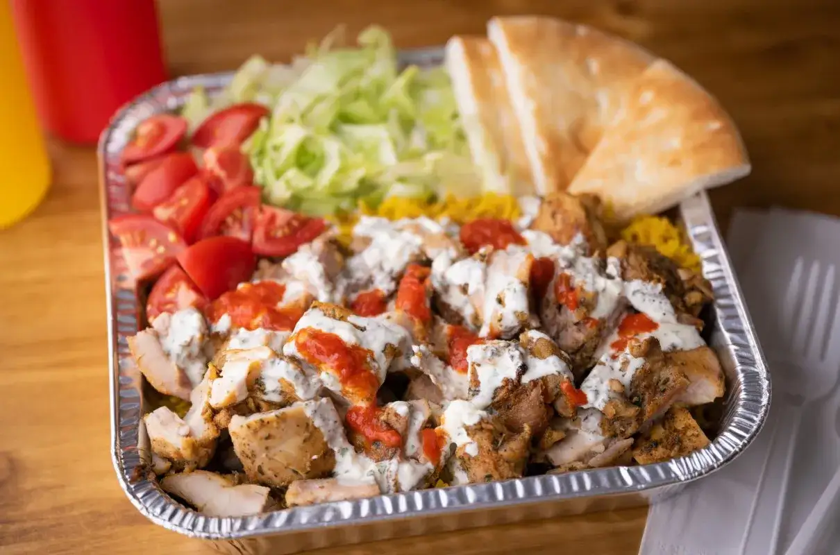 Pyszna shoarma co to? To porcja mięsa z ryżem, pomidorami, sałatą i sosem, podana w aluminiowej tacce.