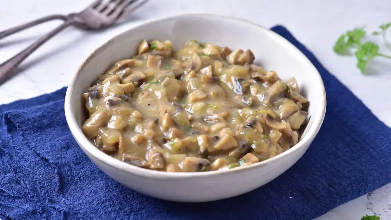 Aksamitny sos pieczarkowy bez śmietany, pełen kawałków grzybów, podany w białej miseczce na granatowej serwetce.