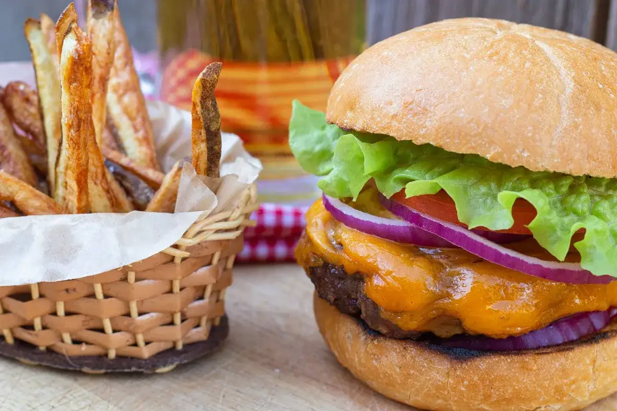 Soczysty burger z serem i frytkami w koszyku, idealny do maczania w sosie amerykańskim.