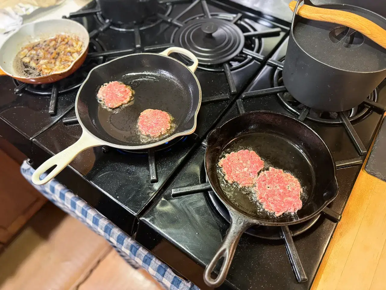 Na patelni smażą się cienkie kotlety, idealne do przygotowania smash burgera. Obok podsmażona cebulka.