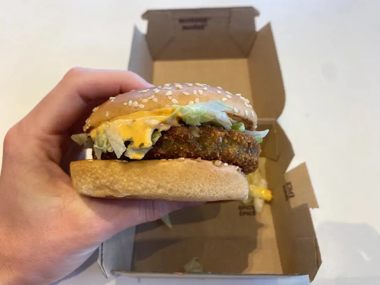 Ręka trzyma wege burgera z McDonald's, z chrupiącym kotletem, sałatą i sosem.