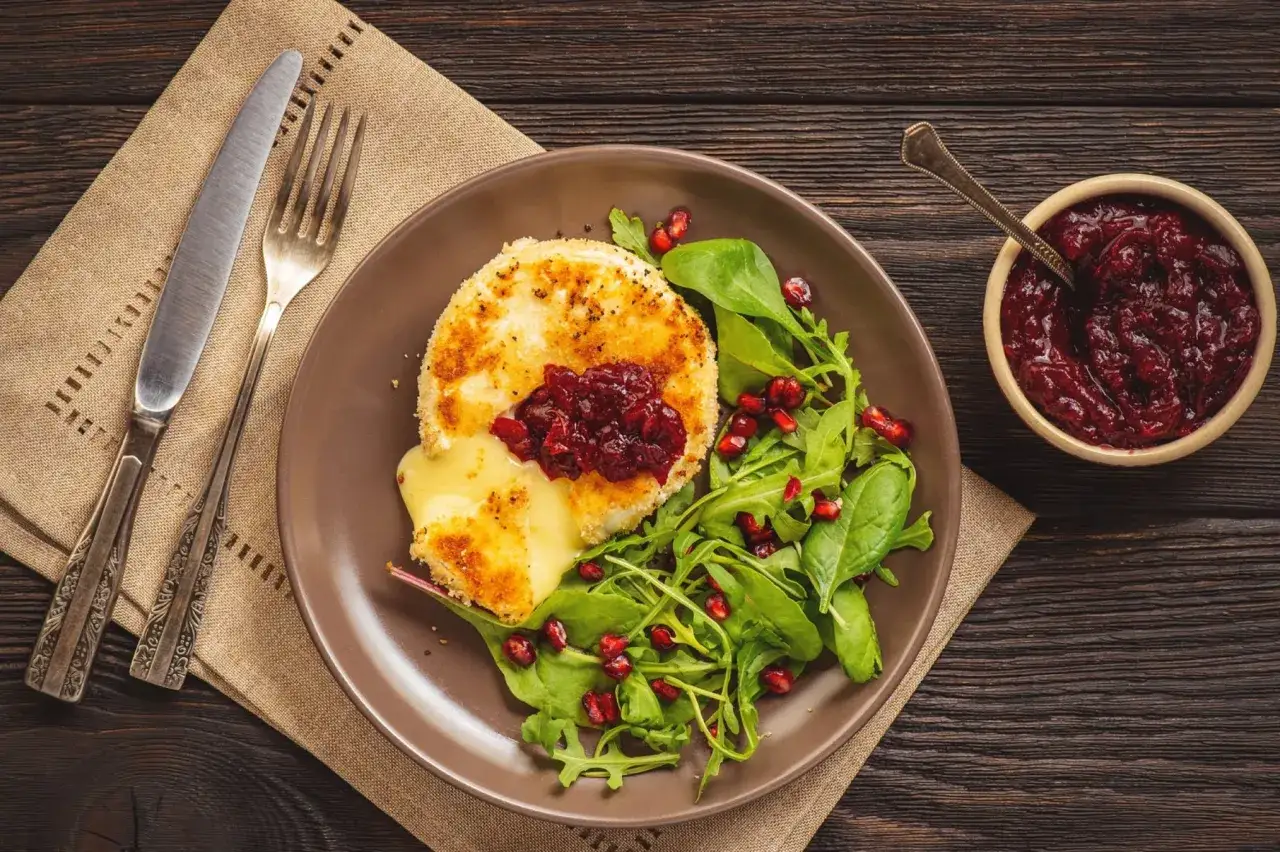 Pyszny camembert w panierce, rozpływający się ser, podany z sałatką z rukoli, szpinaku i granatu, z dodatkiem żurawiny.