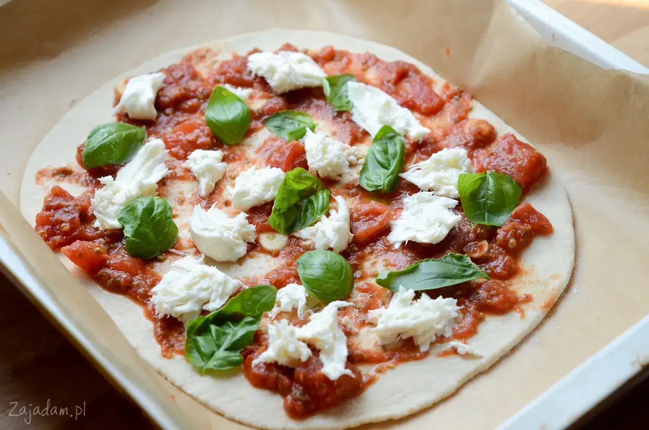Niedopieczona margarita pizza z pomidorami, mozzarellą i bazylią na papierze do pieczenia.