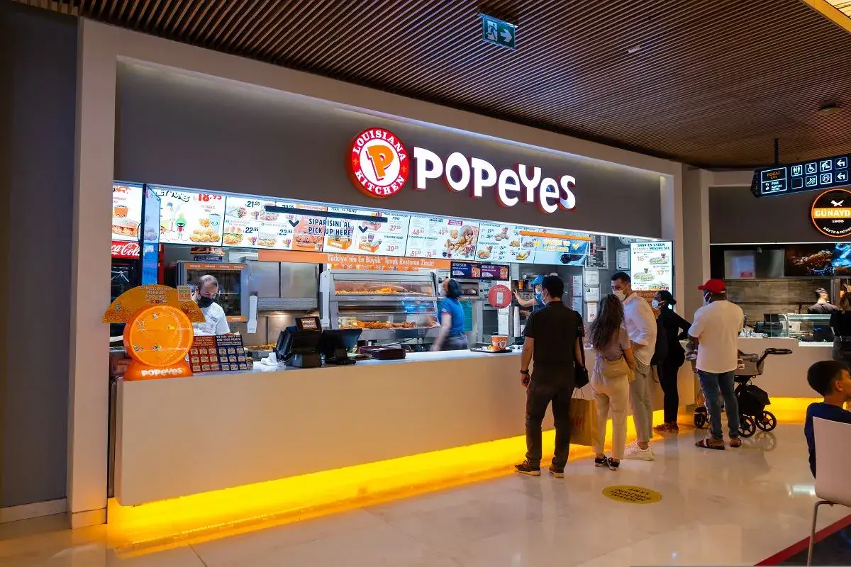 Klienci w Popeyes Polska czekają na zamówienie. W tle menu z daniami i pracownicy restauracji.