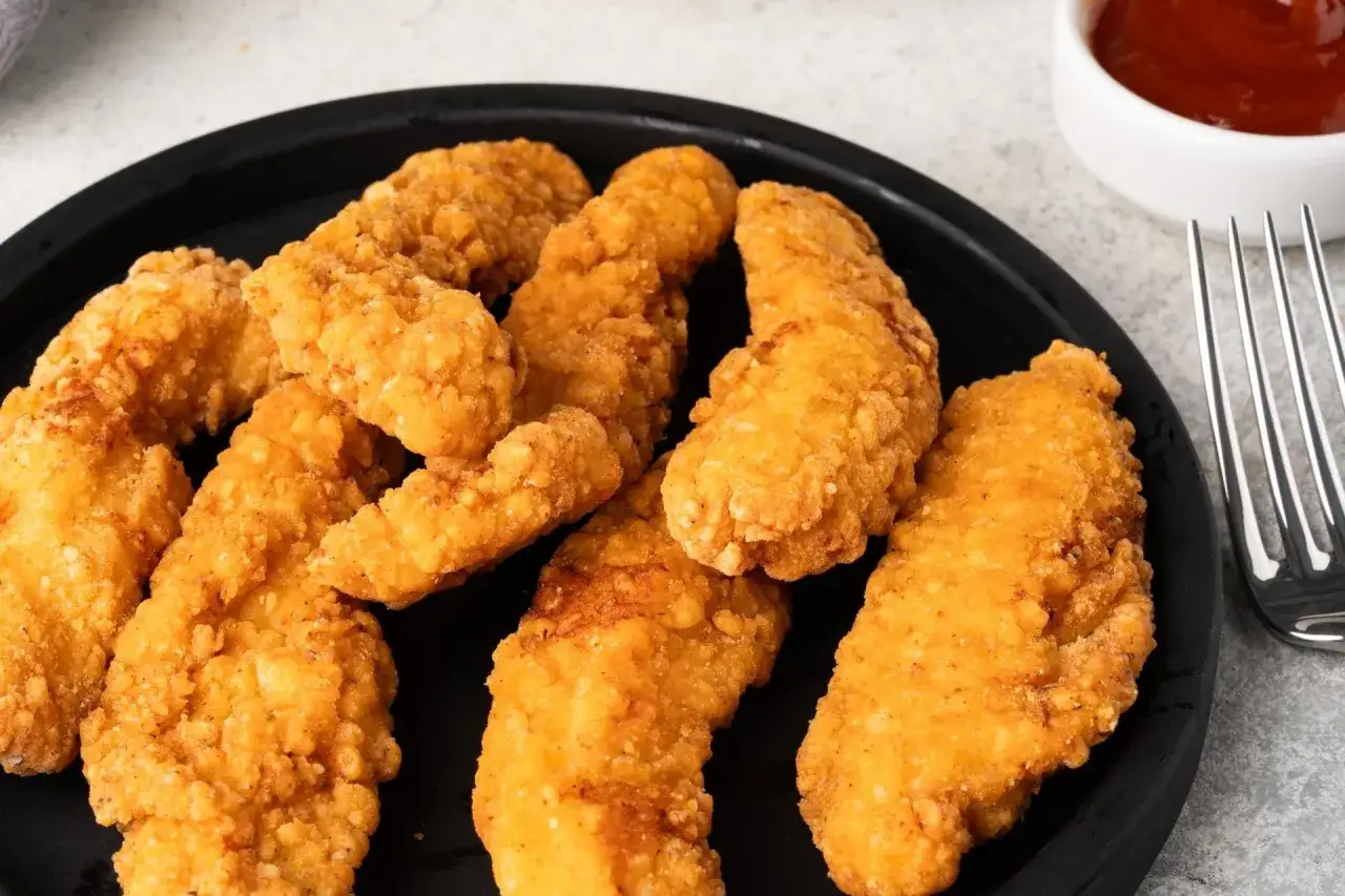 Chrupiące bites KFC na czarnym talerzu, gotowe do zanurzenia w sosie.