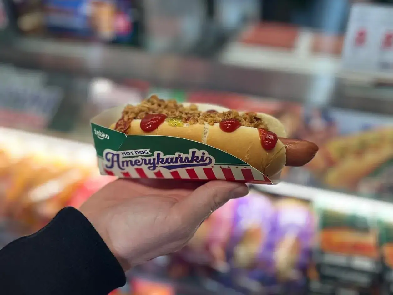 Pyszny hot dog Amerykański z Żabki, z chrupiącą cebulką i ketchupem. Zastanawiasz się, ile kosztuje hot dog w Żabce?