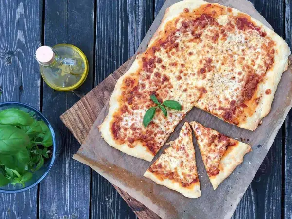 Pyszna margarita pizza z roztopionym serem i świeżą bazylią, obok butelka oliwy i miseczka ziół.